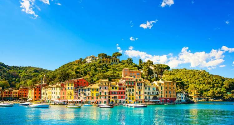 Bunte pastellfarbene Gebäude von Portofino säumen einen funkelnden türkisfarbenen Hafen an einem strahlend sonnigen Tag.