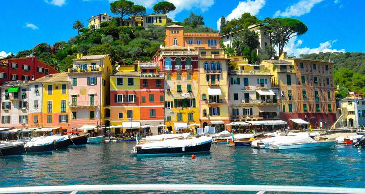 Lebendige pastellfarbene Gebäude säumen einen malerischen italienischen Hafen voller Yachten und klarem blauen Wasser.