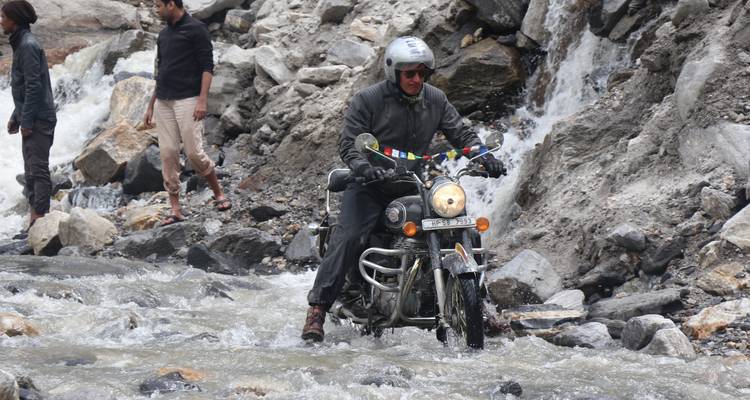 Motocycliste traversant une rivière avec un terrain montagneux.