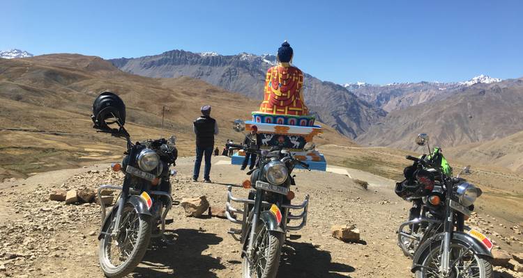 Motos garées devant une statue de Bouddha dans un paysage montagneux.