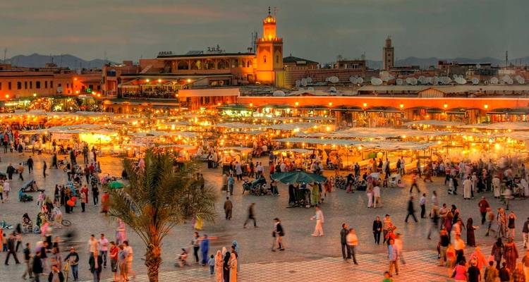 Bulliciosa plaza de Jemaa el-Fna al atardecer, abarrotada de puestos, gente y linternas resplandecientes con un minarete al fondo.