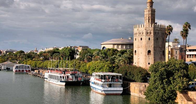 Daytime riverside scene of Torre del Oro with tour boats moored along Seville’s riverbank.
