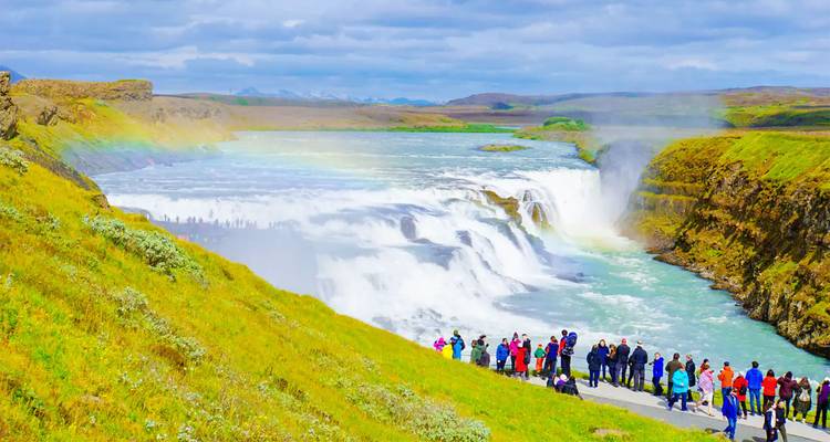 A waterfall with a rainbow and tourists viewing from a distance