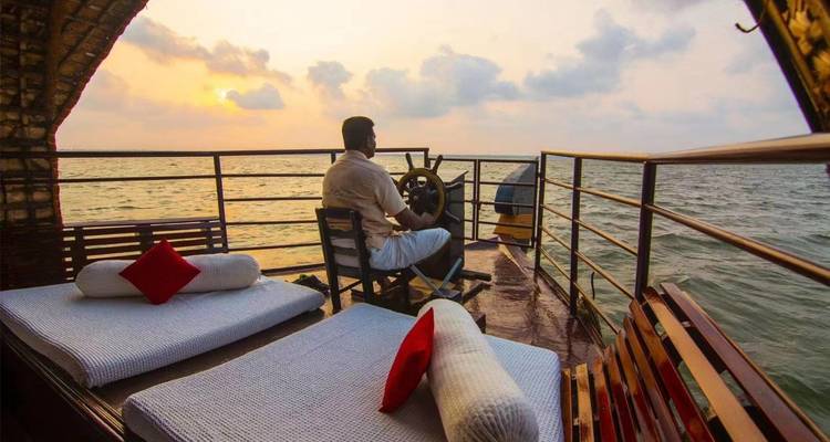 Person, die ein Hausboot bei Sonnenuntergang steuert, mit nahegelegenen Kissen als Sitzgelegenheit.