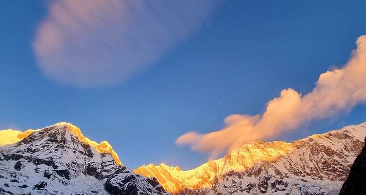 Goldenes Licht, das die Gipfel schneebedeckter Berge vor blauem Himmel beleuchtet.