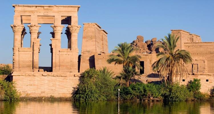 Ruines de temple au bord d'une rivière avec des palmiers.