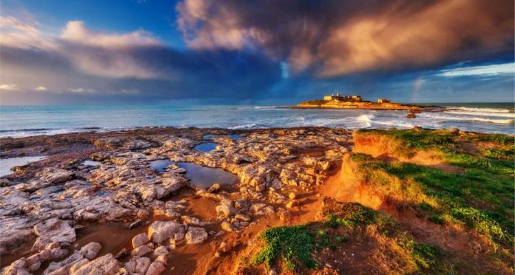 Kustlandschap met dramatische luchten en een afgelegen eiland.
