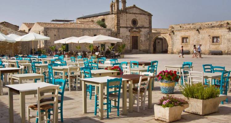 Terrasje op een historisch plein met blauwe stoelen.