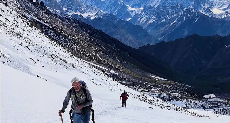 Smiling trekkers climbing snowy slope with dramatic jagged mountain range backdrop.