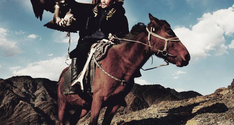 A man on horseback with a bird of prey against a mountain backdrop.