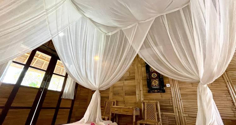 Slaapkamer met bamboe wanden en een hemelbed.