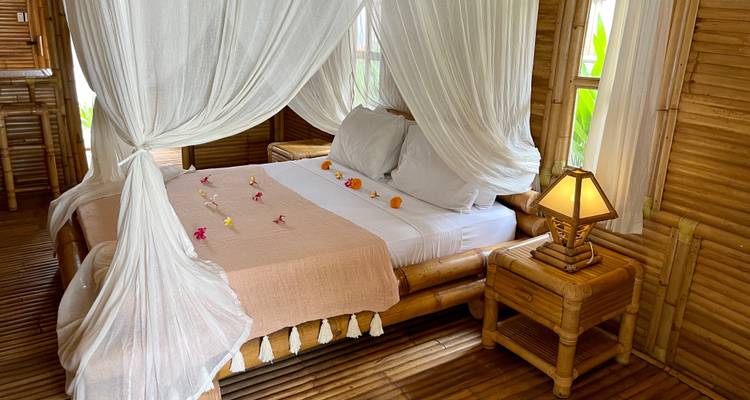 Mooi versierd bed in een kamer met bamboe wanden.