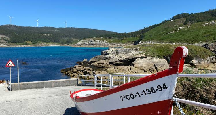 Rode boot aangemeerd bij een rotsachtige kust met windturbines.