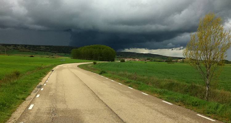 A rural road curving through a green landscape with an ominous dark sky.