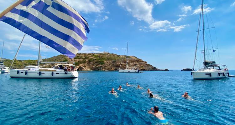 Des gens qui nagent dans la mer avec des voiliers et un drapeau grec.