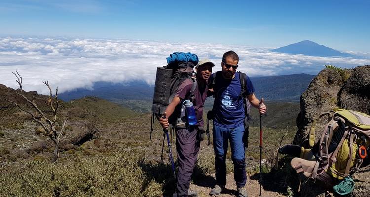 Gruppe von Wanderern auf einem Berg mit Wolken und einem entfernten Gipfel.