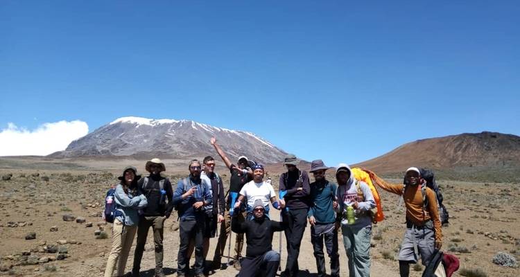 Gruppe posiert vor Bergkulisse, klarer Himmel und felsiger Boden.