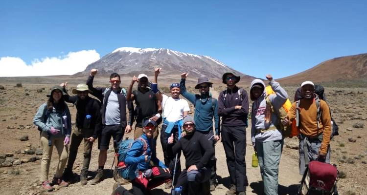 Wandergruppe vor einem Berg, die ihre Fäuste jubelnd in die Höhe streckt.