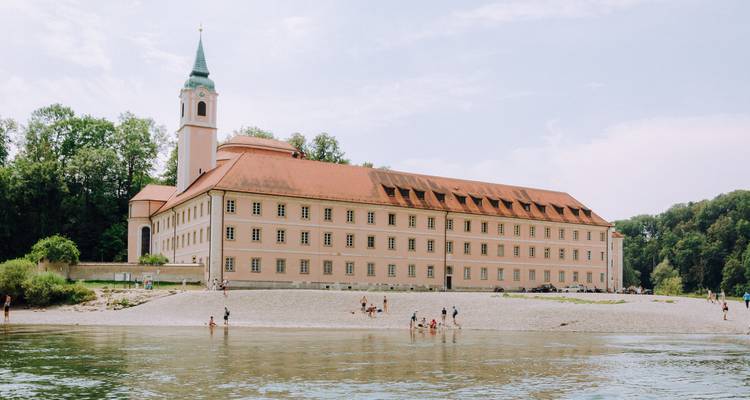 Groot historisch gebouw naast een rivier met mensen die genieten van het strand.