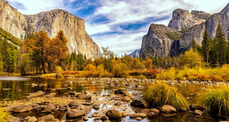 Herbstfarben im Yosemite Valley mit aufragenden Granitwaenden und dem Merced River im Vordergrund.