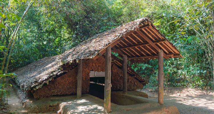 Thatched wooden bunker entrance nestled in dense jungle at the Cu Chi historical site.