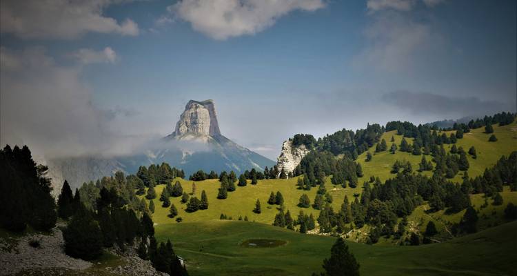 Majestuosa cima montañosa rodeada de valles frondosos y nubes ondulantes.