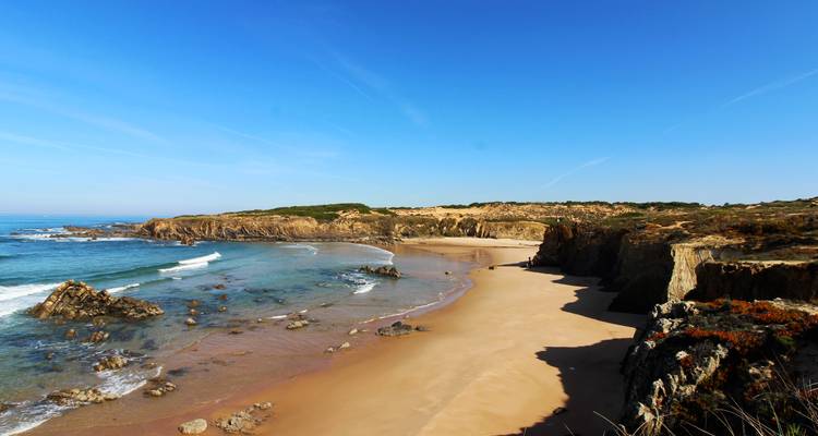 Sandy beach with rocky cliffs and clear waters.