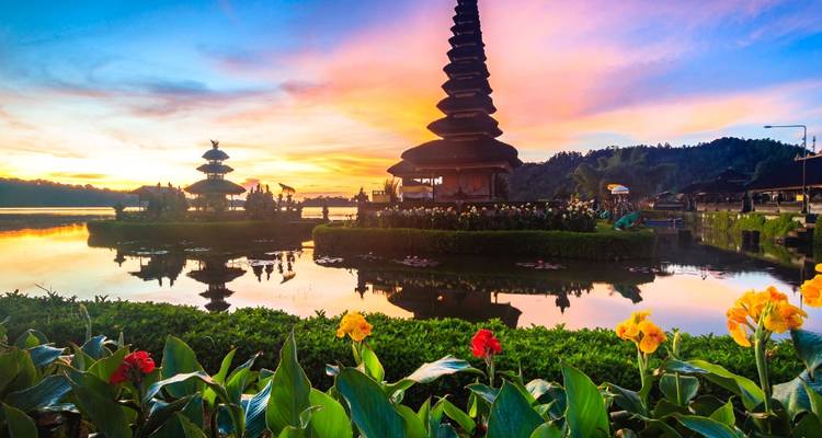 Sunset view of a temple on a lake surrounded by flowers.