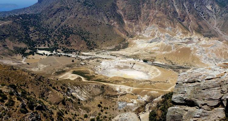 Vista aérea de una gran cuenca de cráter volcánico rodeada por montañas escarpadas y árboles dispersos