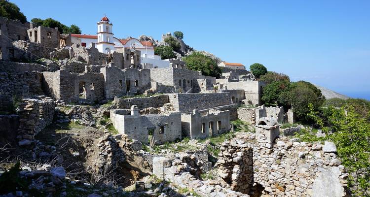 Ruinas de piedra de un pueblo abandonado en la ladera con iglesia blanca y cielo azul de fondo