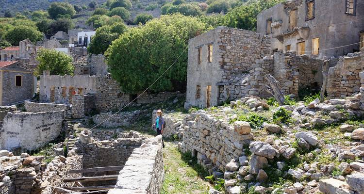 Viajero caminando entre escombros de piedra y vegetación crecida en un entorno de pueblo abandonado