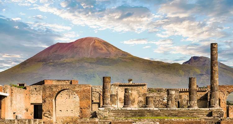 Ruïnes van Pompeii met staande zuilen tegen de achtergrond van de Vesuvius onder een gedeeltelijk bewolkte hemel.
