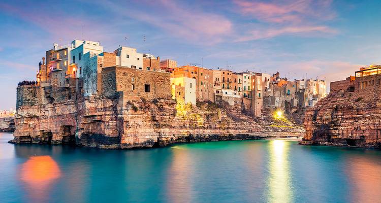 Dramatische kustplaats gelegen op ruige kalkstenen kliffen die gloeien bij zonsondergang boven turquoise wateren.