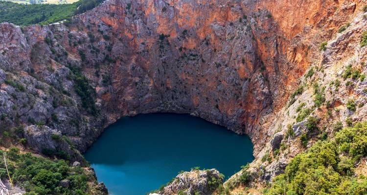 Vista aérea espectacular del profundo Lago Azul de Imotski rodeado de acantilados de color naranja muy pronunciados.