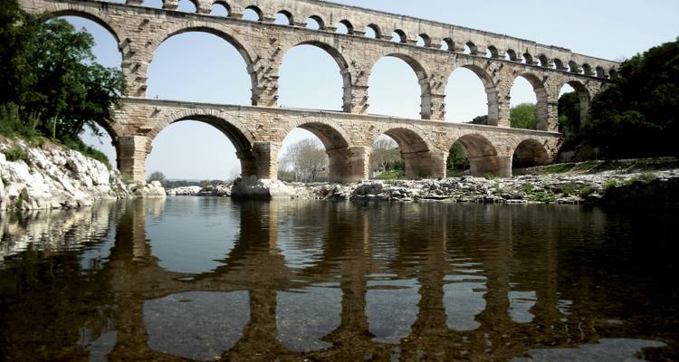 Uralte Steinbögen des Pont du Gard Aquädukts spiegeln sich im klaren Fluss darunter wider.