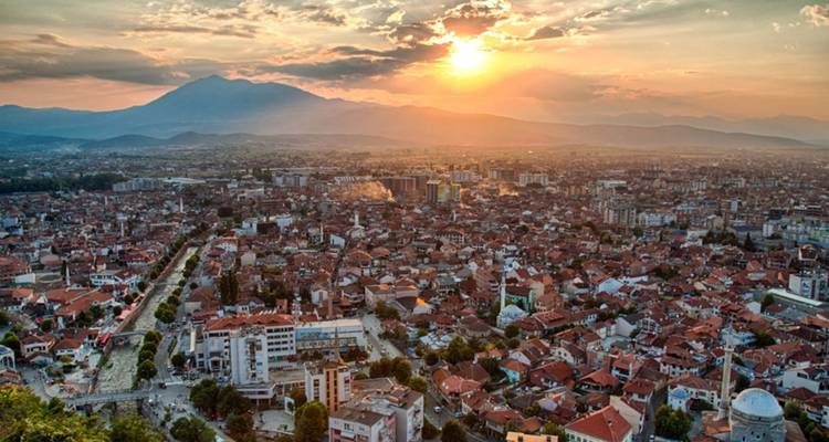 Eine Stadtlandschaft bei Sonnenuntergang mit Bergen im Hintergrund.