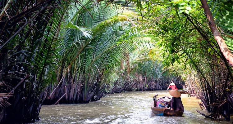Des personnes pagayant dans une embarcation étroite à travers une végétation tropicale luxuriante dans un canal.