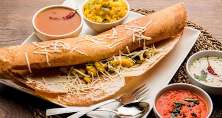 Ein Teller mit indischem Essen mit einer großen Dosa und mehreren Beilagen.