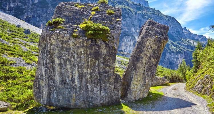 D'énormes blocs rocheux fendus se dressent à côté d'un sentier de gravier dans une vallée alpine spectaculaire du Tyrol.