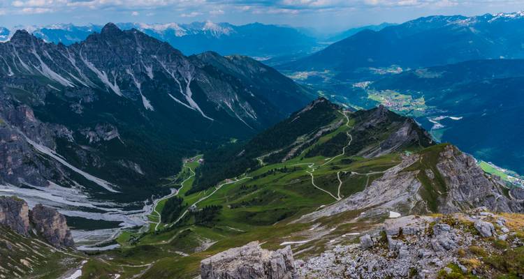 Des crêtes de haute altitude et des sentiers serpentins serpentent à travers un paysage alpin spectaculaire sous des nuages épars.