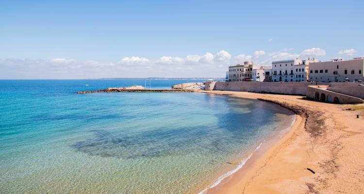 Kristallklares türkisfarbenes Meer, das einen sandigen Strand unterhalb der weiß getünchten Mauern von Gallipoli umspült