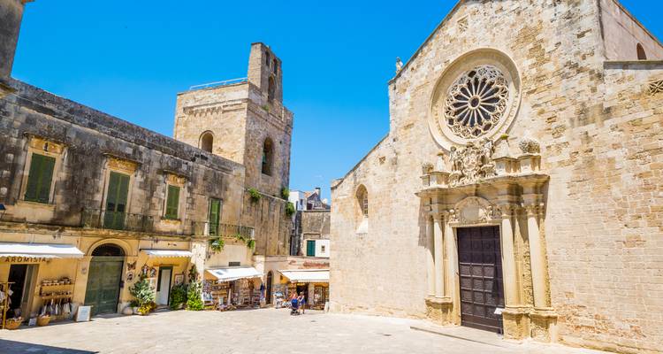 Fachada de catedral de piedra iluminada por el sol y plaza tranquila en un pueblo del sur de Italia