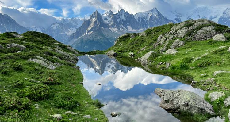 Un lago alpino cristalino que refleja perfectamente los picos irregulares cubiertos de nieve del macizo del Mont Blanc bajo un cielo parcialmente nublado.