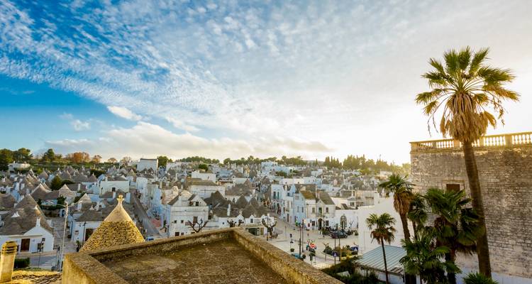 Een panoramisch uitzicht op Alberobello's witgekalkte trulli-huizen onder een heldere hemel met uitgestrekte wolken.