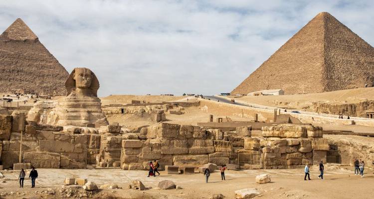 The Sphinx and two pyramids with visitors in the foreground.