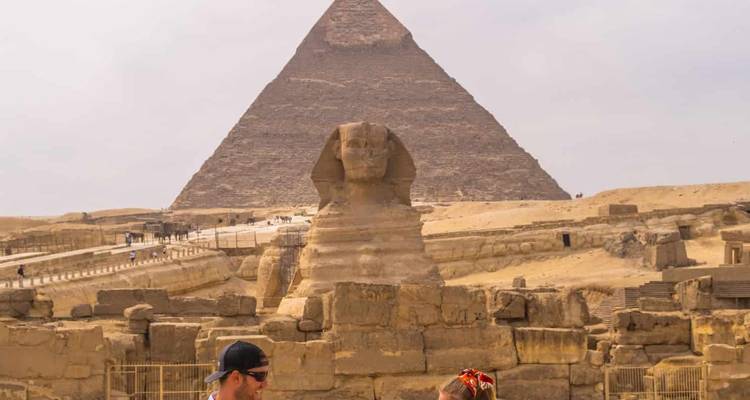 The Sphinx and a pyramid with tourists in the foreground.