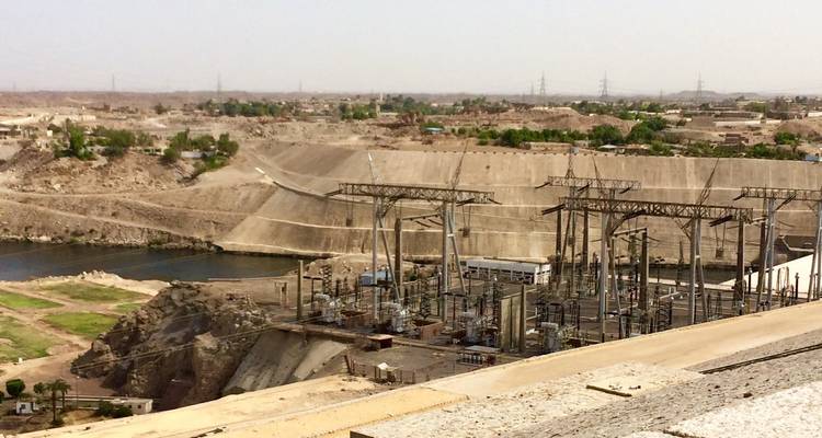 Wide view of a massive concrete dam and power station installation on a desert river.