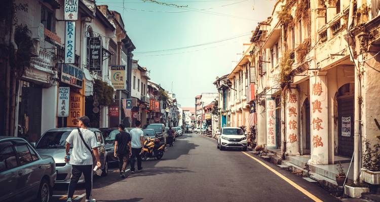 Rue historique bordée de maisons-boutiques avec des voyageurs marchant parmi les motocyclettes garées sous une lumière chaude.