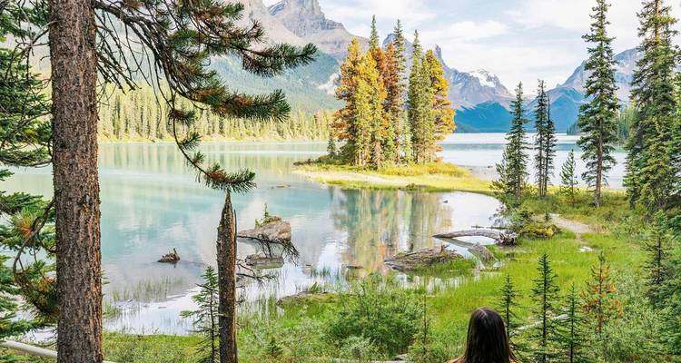 Un visiteur solitaire contemple le lac Maligne turquoise et l'île Spirit boisée avec les montagnes Rocheuses déchiquetées au-delà.