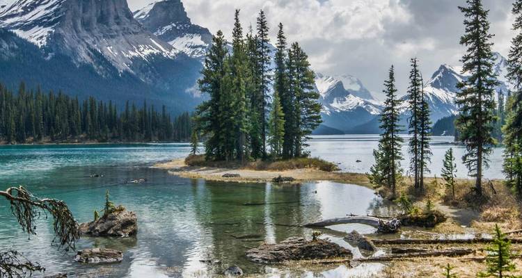Lago turquesa cristalino que rodea una pequeña isla cubierta de pinos bajo picos escarpados espolvoreados de nieve.